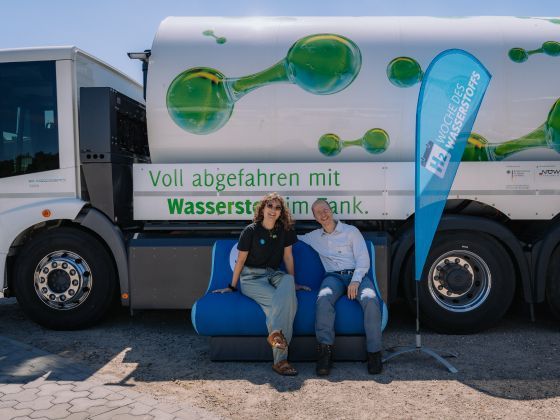 Lillian Hurth (links) und Moritz Sanne (rechts) sitzen vor einem Wasserstoff-Abfallsammelfahrzeug der BDG auf dem Wasserstoff-Sofa von der Woche des Wasserstoffs in Bernau bei Berlin (Foto: JACKZ Productions/WDW)